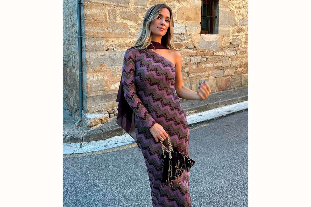 María Pombo con vestido asimétrio de estampado geométrico en color burdeos y bolso de mano