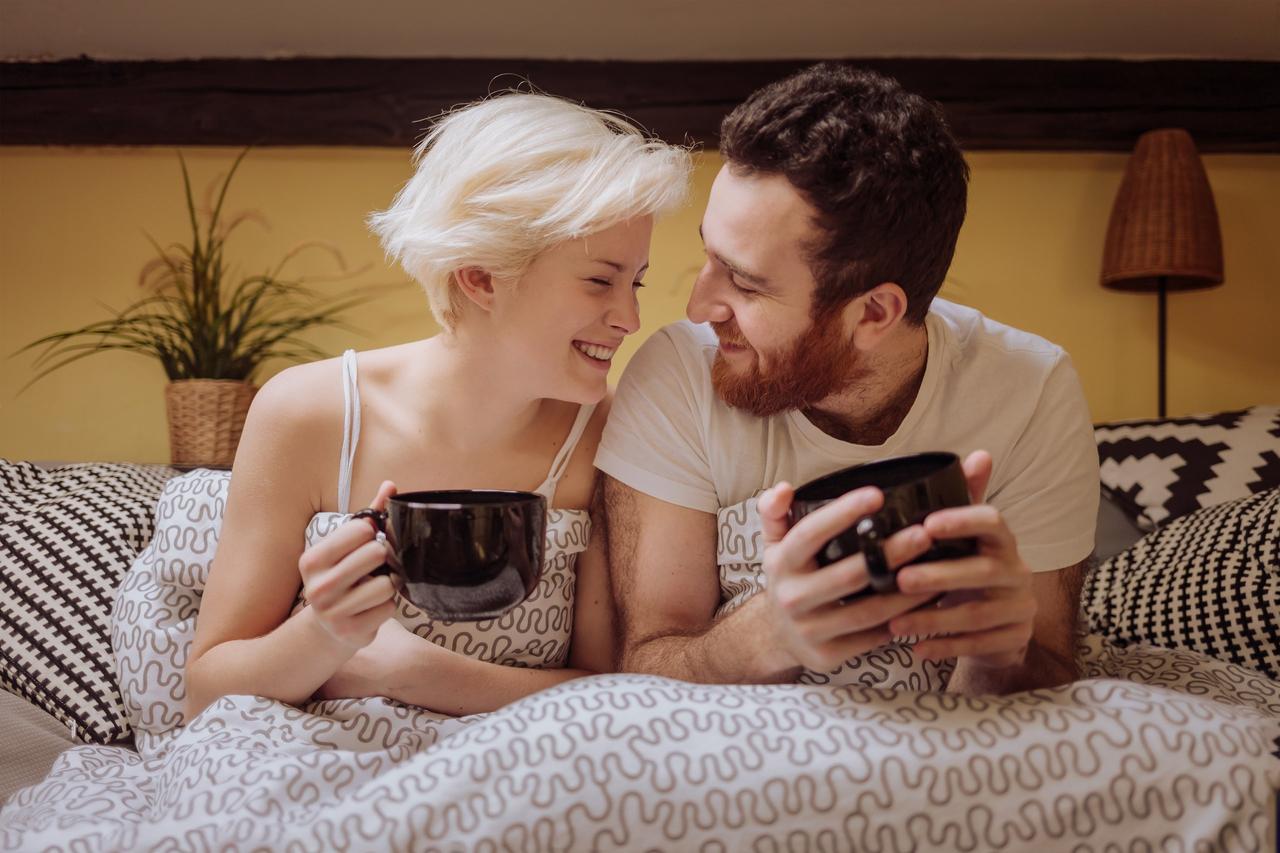 Regalos para novios: pareja sentada en una cama o sofá con una taza negra en la mano cada uno