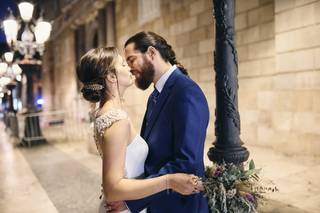 Pareja vestida de novios a punto de darse un beso en una calle durante la sesión de fotos postboda