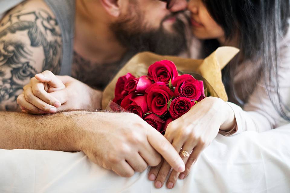 pareja besándose en la cama con un ramo de rosas