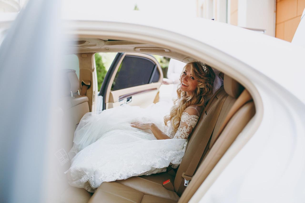 Chica vestida de novia, muy sonriente y con la melena suelta en el interior de un coche blanco