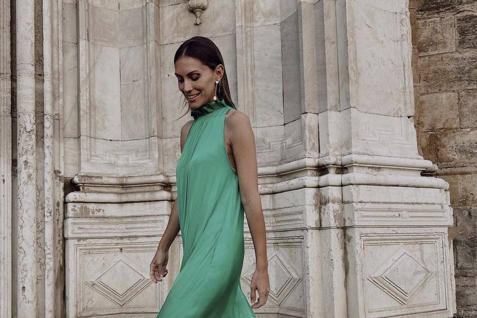 Chica sonriente con el pelo suelto peinado hacia atrás lleva un vestido verde sin mangas y unos bonitos pendientes largos