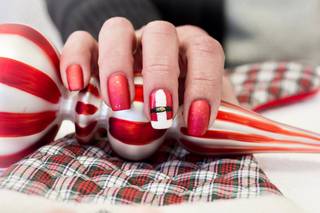 Diseño de uñas navideñas 2024: manicura en rojo con brillos y uña decorada de Papá Noel