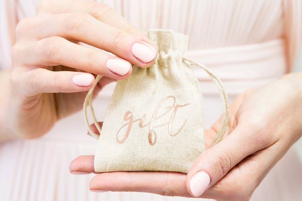 Manos de mujer con las uñas pintadas de rosa sujetan un saquito de fibras naturales con la palabra Gift escrita