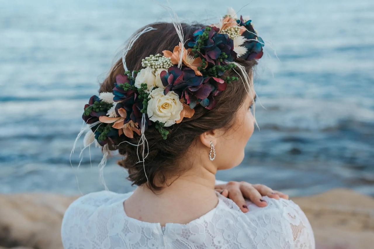 Chica de espaldas delante del mar con un recogido clásico y una corona para novia de flores sofisticada