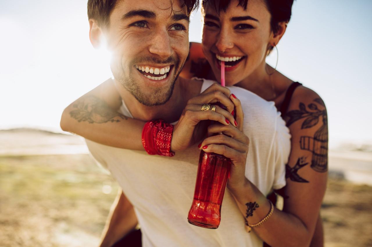 Cosas que los hombres quieren de su relación: risas y complicidad. Chico y chica jóvenes y muy sonrientes, mientras él la lleva a ella a caballito