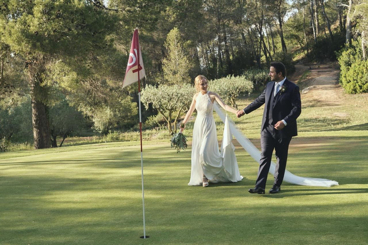 Aniversarios de boda: pareja de recién casados pasean felices y cogidos de la mano por un campo de golf