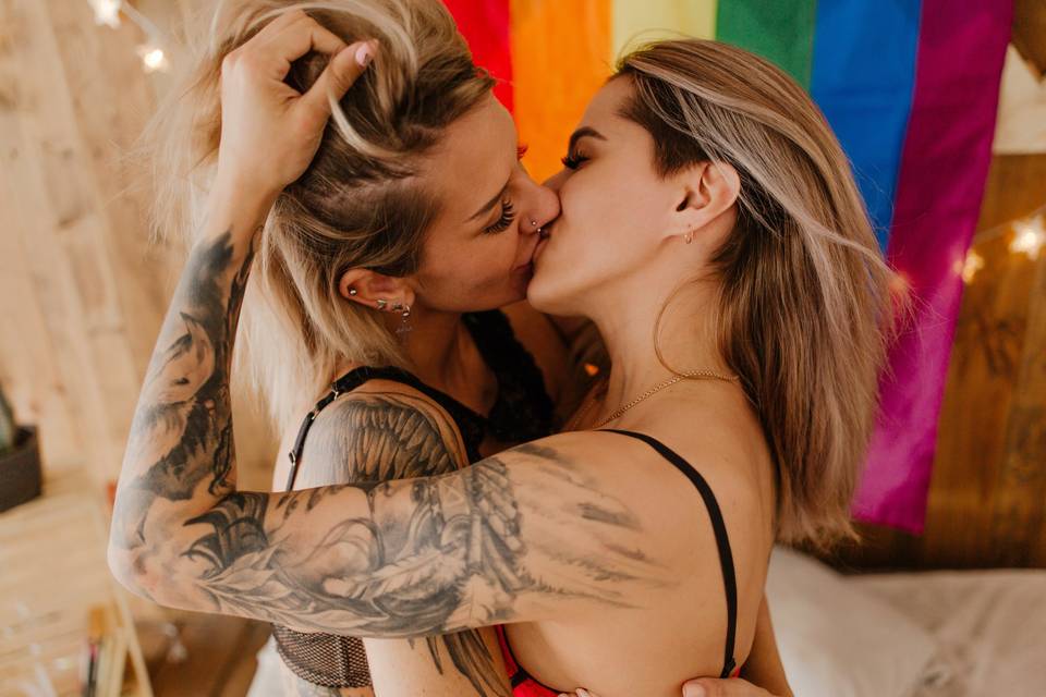 Parejas de famosos homosexuales: dos chicas se besan apasionadamente delante de una bandera LGBTI+