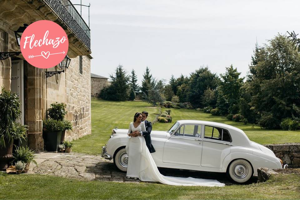 Pazos bodas Galicia: pareja de recién casados se abraza delante de un coche clásico y de un edificio con fachada de piedra