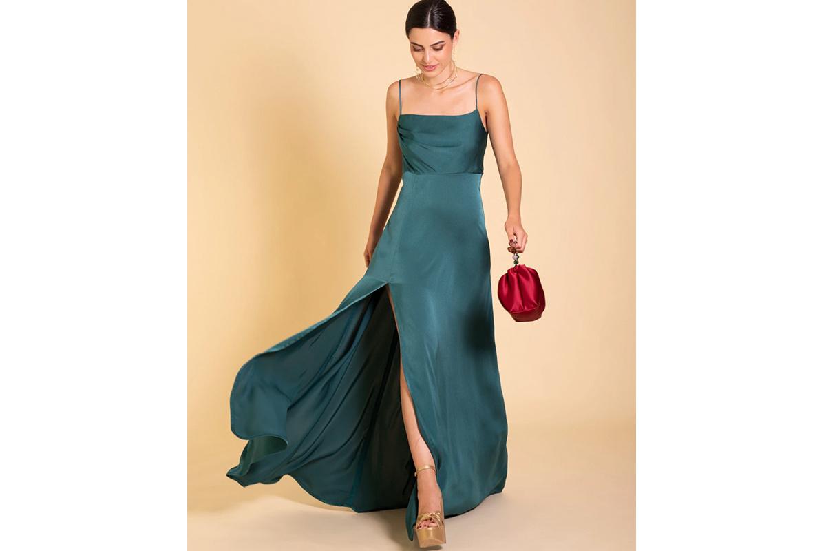 Chica con el pelo recogido con un vestido de fiesta verde con tirantes espagueti, sandalias doradas y bolso rojo en una mano