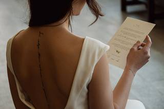 Chica de espaldas con un vestido blanco leyendo un papel que sujeta con una de sus manos