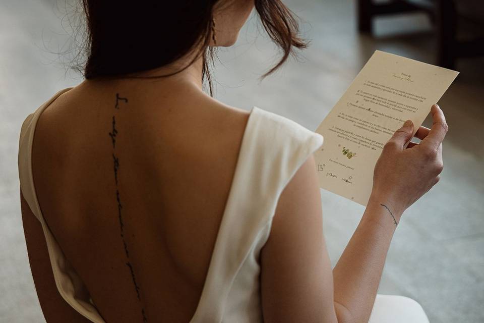 Chica de espaldas con un vestido blanco leyendo un papel que sujeta con una de sus manos