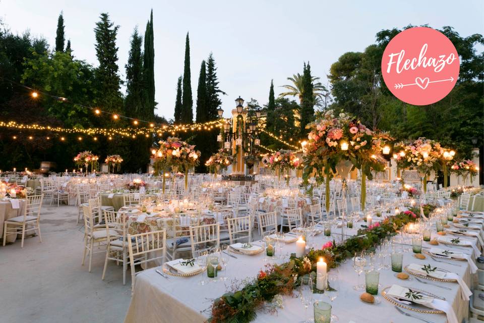 Montaje banquete de boda en tonos blancos en un espacio natural al aire libre decorado con luces cálidas