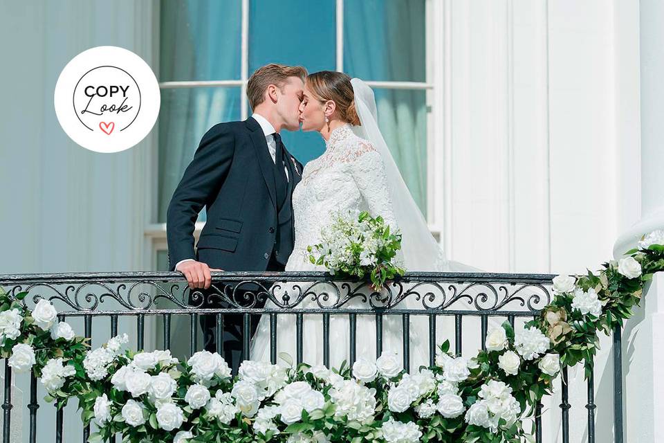 Naomi Biden y Peter Neal besándose en un balcón decorado con flores verdes y blancas