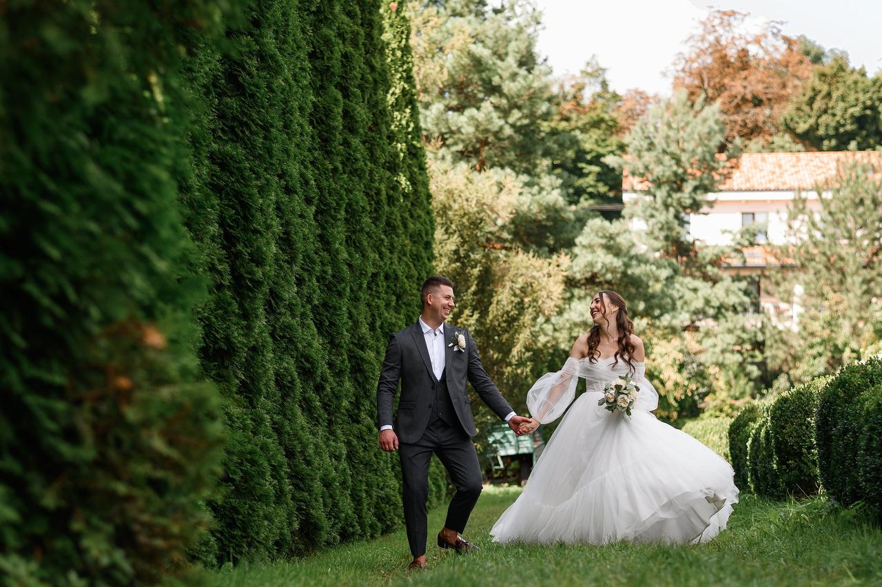 Mentiras de las mujeres: chico con traje clásico y chica con vestido de novia de corte princesa caminan sonrientes y cogidos de la mano