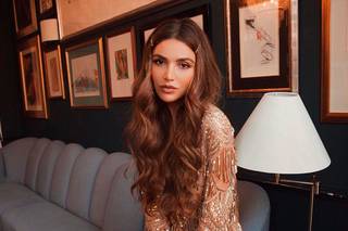 Negin Mirsalehi en un salón lleno de marcos de fotos con el cabello largo peinado con raya en medio y horquillas