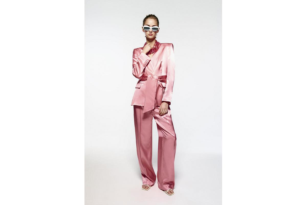 Chica con el pelo recogido y gafas blancas con un conjunto de americana y pantalón satinados en una tonalidad rosa