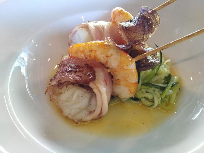 Rape y langostinos con bacon en brocheta sobre tallarines de calbacin y puerro, esencia de gamba roj