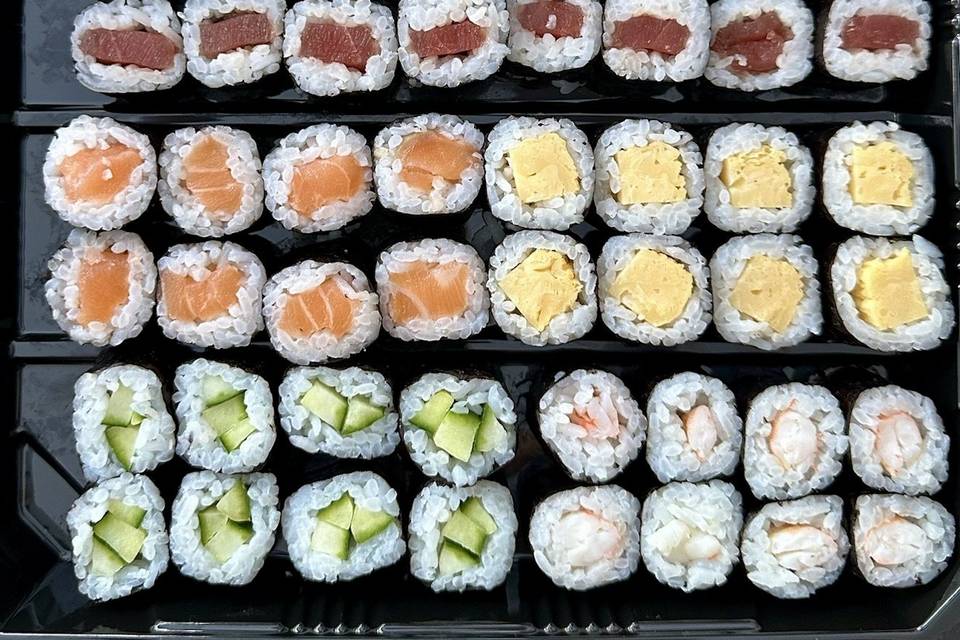 Selección de makis variados de atún, salmón y tamago, presentada en su caja de reparto tal y como llega a tu evento: frescura y sabor en cada bocado.